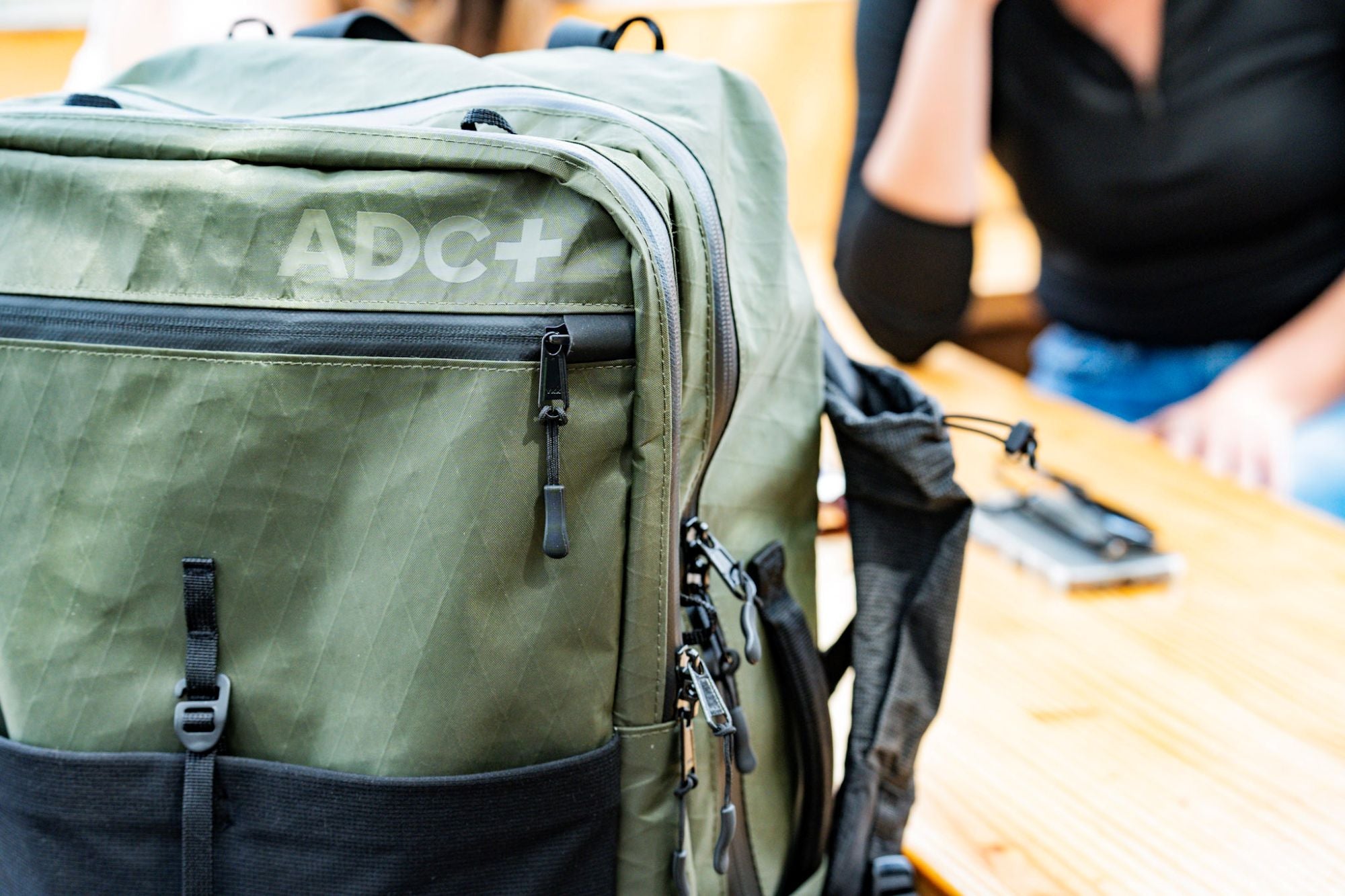 ADC travel backpack in moss color at a table